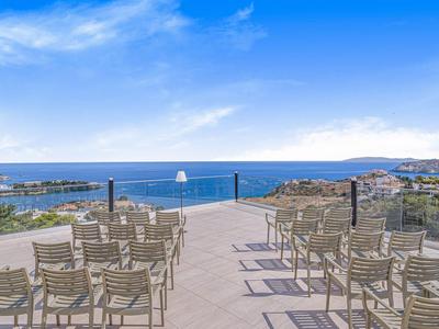 Slunná střešní terasa s židlemi s výhledem na modré moře a přímořské město.