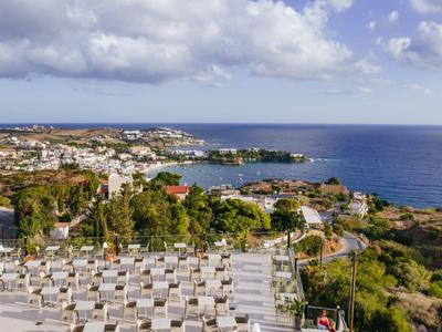 Pohled na přímořské město s domy, vegetací a mořem pod oblačnou oblohou.