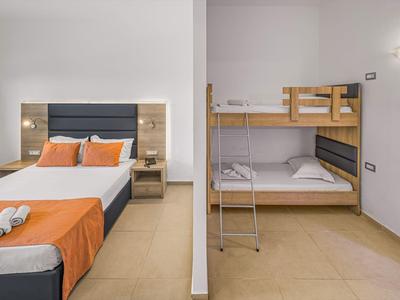 Moderní hotelové pokoje s manželskou postelí a patrovou postelí, jednoduše zařízené s oranžovým ložním prádlem.