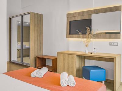 Moderní hotelový pokoj s zrcadlovou skříní, psacím stolem a oranžovou přikrývkou.