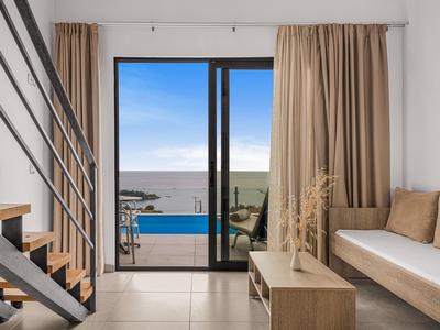 Moderní obývací pokoj se schodištěm a výhledem na bazén a moře přes velké skleněné dveře.