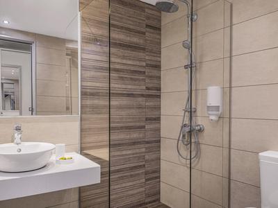 Moderní koupelna s umyvadlem, zrcadlem, sprchou se skleněnou stěnou a toaletou