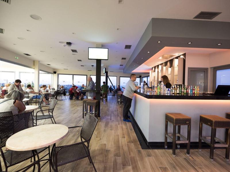 Jasná kavárna s stoly, židlemi a barem s barovými židličkami.