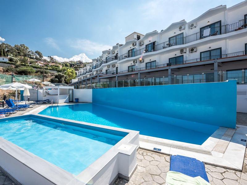 Moderní hotelový bazén se schody a sluneční terasou před vícepodlažním komplexem budov.