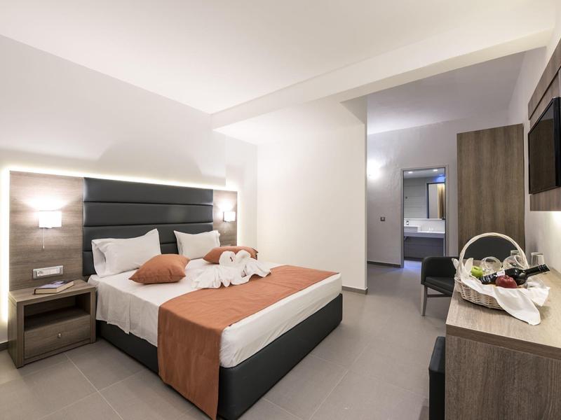 Moderní, světlý hotelový pokoj s velkou postelí a stolem, zdobený květinami.