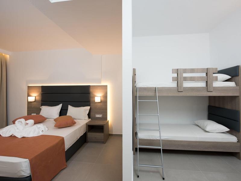 Moderní hotelový pokoj s manželskou postelí a palandami, světlé stěny a minimalistický design.