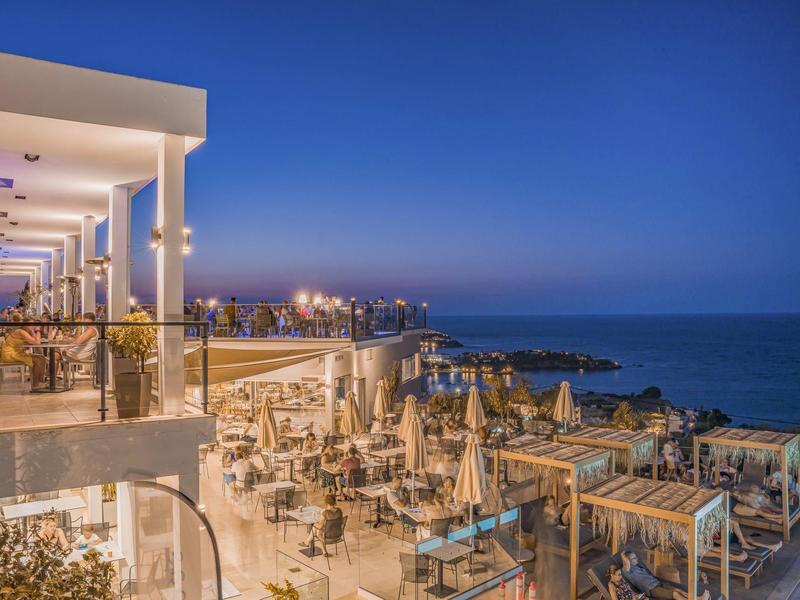 Večerní pohled na rušnou hotelovou terasu s výhledem na moře a čistou oblohu.
