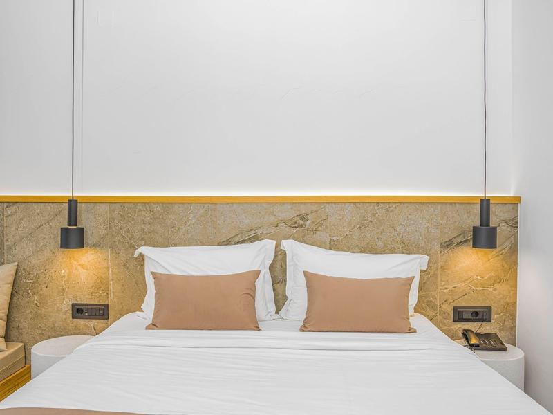 Moderní hotelový pokoj s velkou manželskou postelí, pohodlnými polštáři a závěsnými nočními lampami.