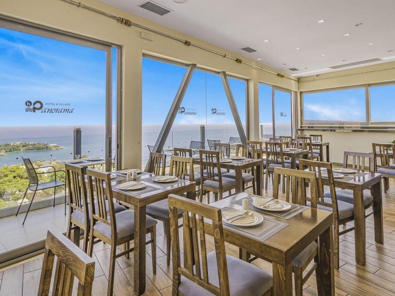 Světlá restaurace se dřevěnými židlemi, stoly a velkým výhledem na moře přes okna od podlahy ke stropu.