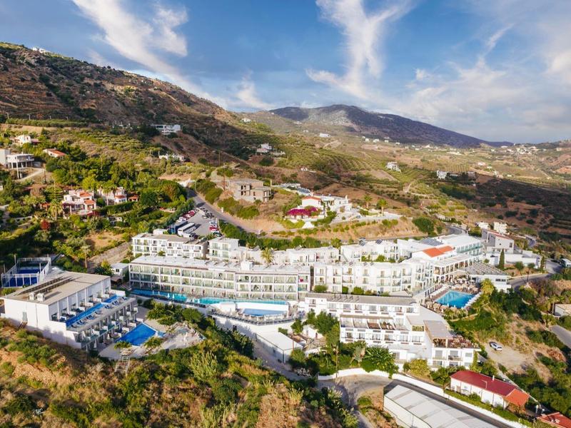 Velký hotelový komplex s bazény na slunném kopci v venkovském prostředí.