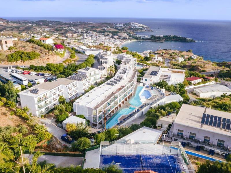 Letecký snímek resortu s několika budovami, bazény a výhledem na moře.