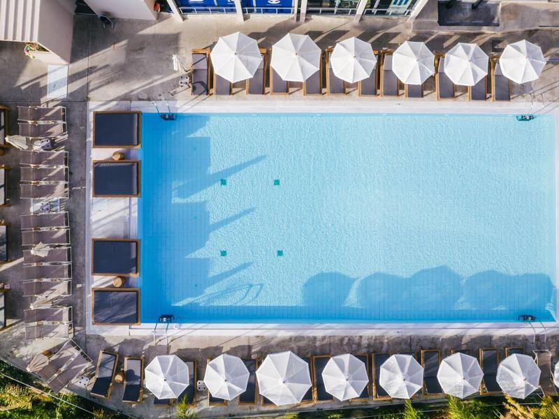 Obdélníkový bazén s bílými slunečníky a lehátky na dlážděné terase.