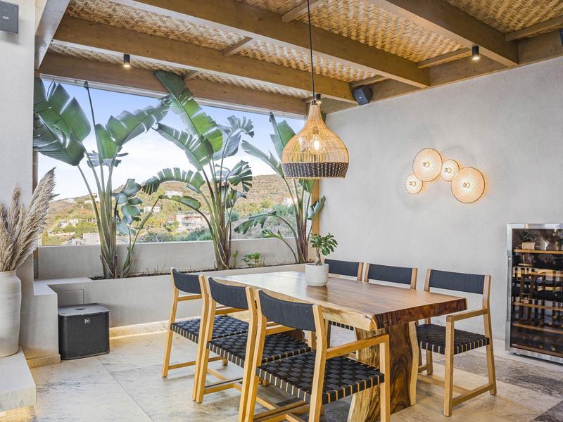 Otevřená jídelní část s dřevěným stolem, židlemi, rostlinami a moderním osvětlením na terase.