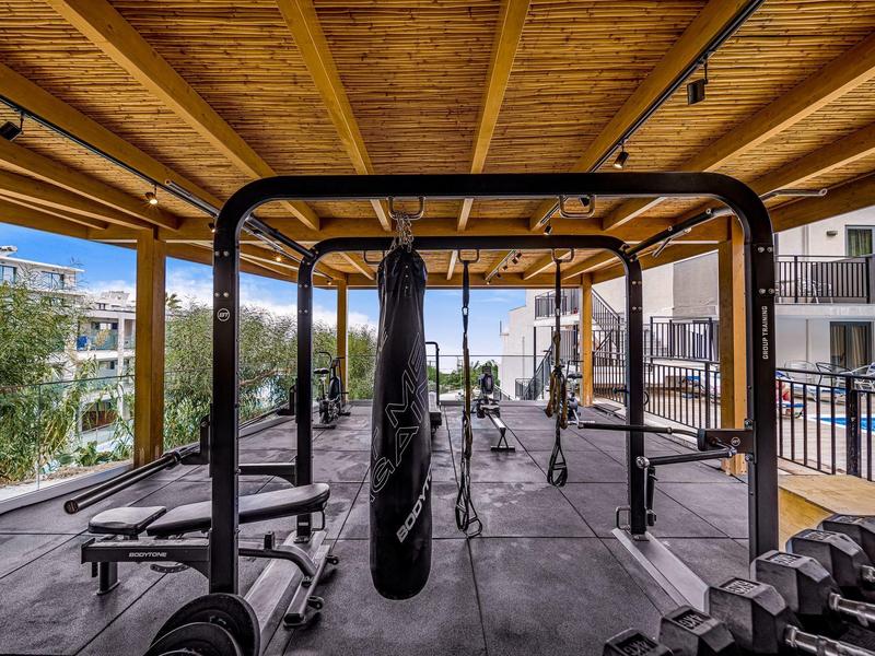 Krytá venkovní fitness zóna s boxovacím pytlem, závažími a posilovacími stroji pod dřevěným stropem.