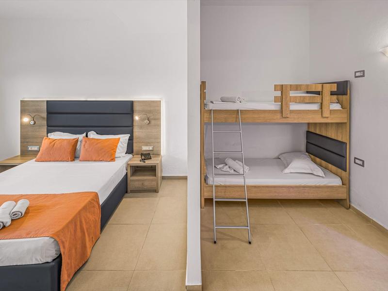 Moderní hotelové pokoje s manželskou postelí a patrovou postelí, jednoduše zařízené s oranžovým ložním prádlem.