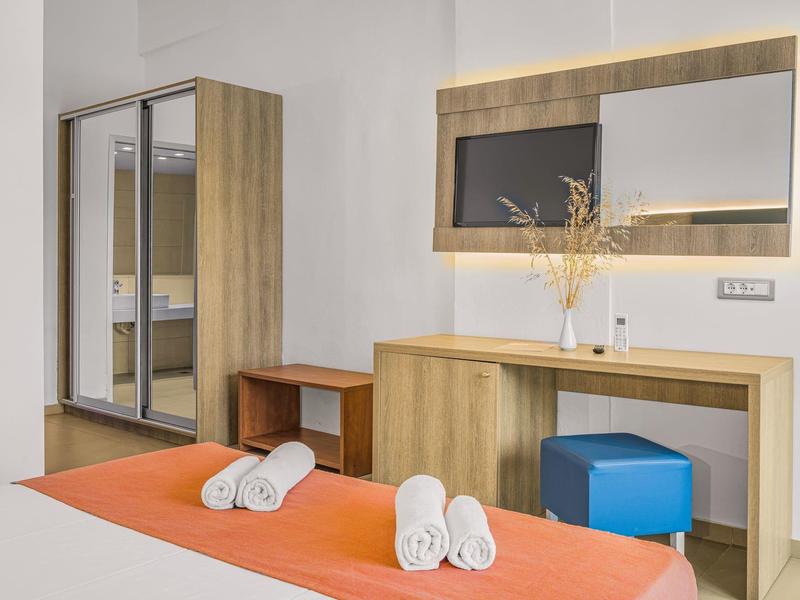 Moderní hotelový pokoj s zrcadlovou skříní, psacím stolem a oranžovou přikrývkou.