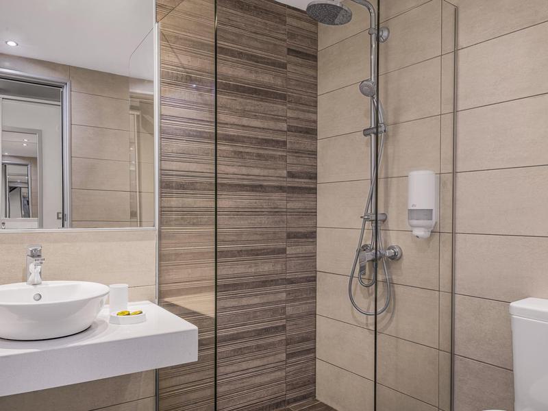 Moderní koupelna s umyvadlem, zrcadlem, sprchou se skleněnou stěnou a toaletou