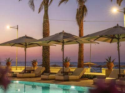 Ligbedden met parasols en palmbomen op het strand bij zonsondergang.