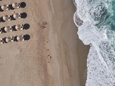 Luftaufnahme eines Strandes mit Liegestühlen und Sonnenschirmen neben brechenden Wellen