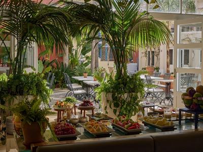 Innenraum eines Cafés mit großen Pflanzen und einem Buffet mit verschiedenen Speisen.