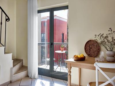 Heller Raum mit Treppe, Glastür zum Balkon, Holztisch mit Obst und dekorativen Vasen.