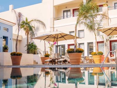 Gezellig buitenzwembad met parasols en palmbomen voor een hotelgebouw.
