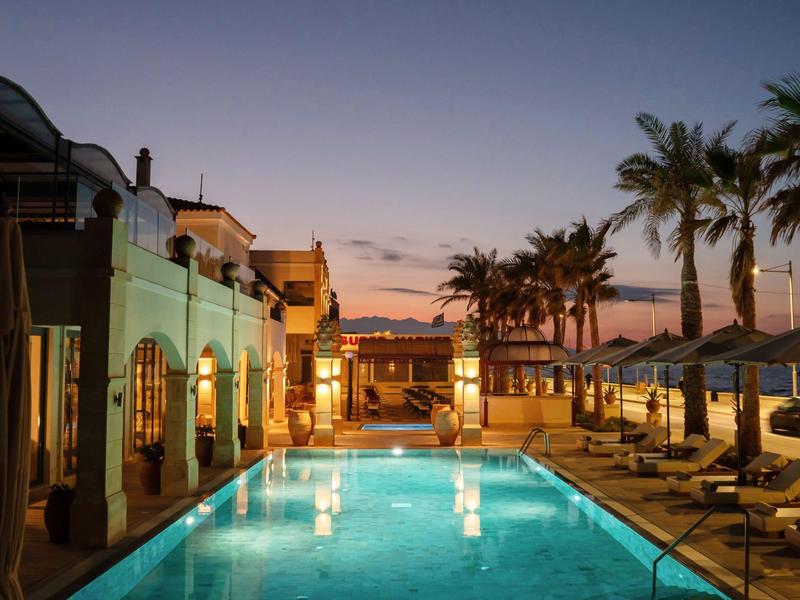 Abendlicher Hotelpool mit beleuchteten Liegestühlen und Palmen unter klarem Himmel