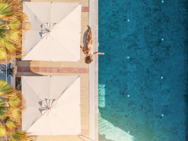 Drohnenaufnahme eines Schwimmbads mit zwei Sonnenschirmen und einer Person am Beckenrand