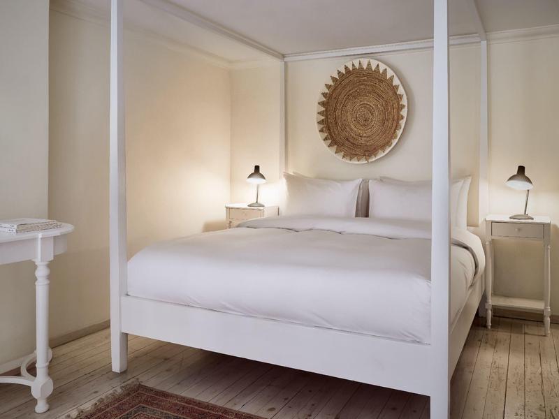 Weißes Himmelbett mit weißer Bettwäsche in einem hellen Schlafzimmer und Wanddekoration aus Holz.