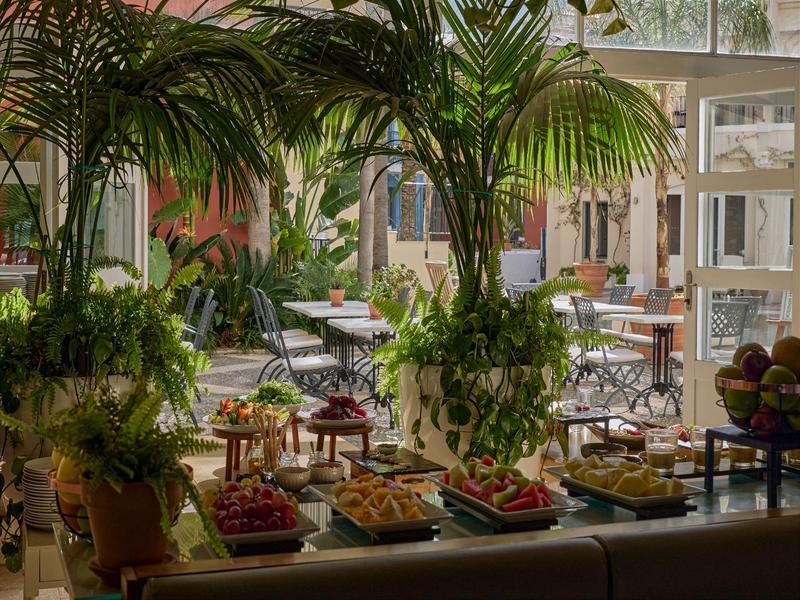 Innenraum eines Cafés mit großen Pflanzen und einem Buffet mit verschiedenen Speisen.