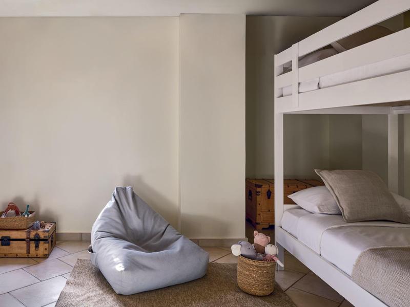 Einzimmer mit graßblauem Sitzsack, Etagenbett, Holzkisten und einfachem weißen Wandhintergrund.