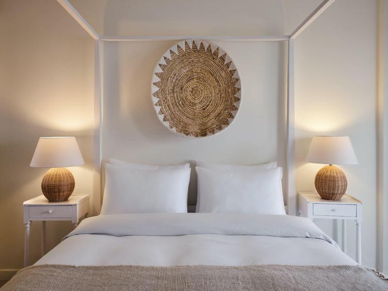 Schlichtes Hotelzimmer mit Doppelbett, weißen Kissen, zwei Nachttischen und runden Lampen.