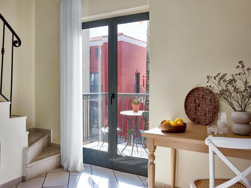 Heller Raum mit Treppe, Glastür zum Balkon, Holztisch mit Obst und dekorativen Vasen.