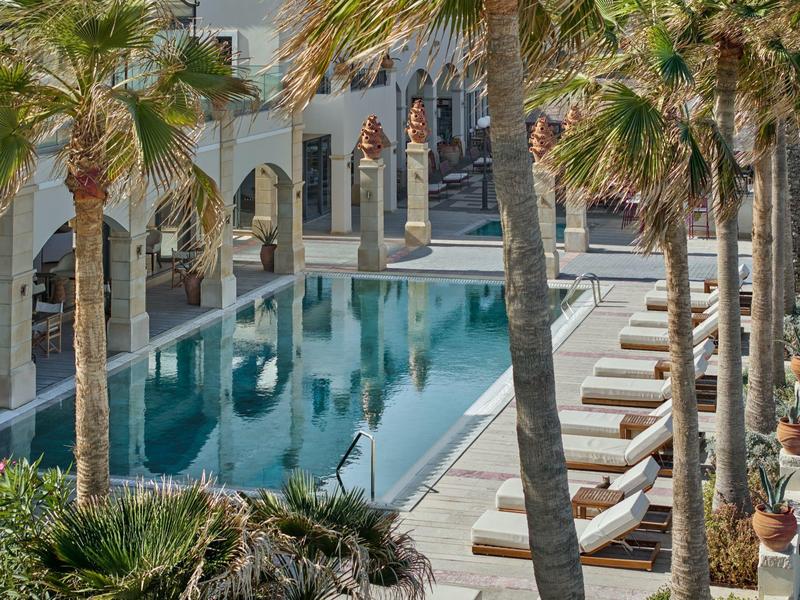 Eleganter Außenpool mit Palmen, Liegestühlen und Laubengängen in einem modernen Hotelgarten.