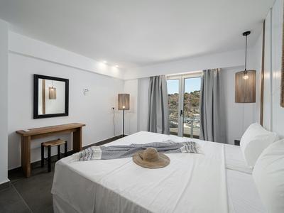 Lichte hotelkamer met tweepersoonsbed, twee lampen en raam met uitzicht op heuvels.