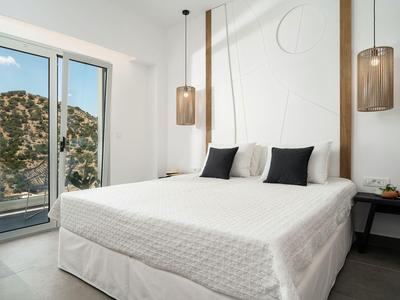 Moderne slaapkamer met groot bed, witte muren en twee hanglampen naast een raam met uitzicht op bergen.