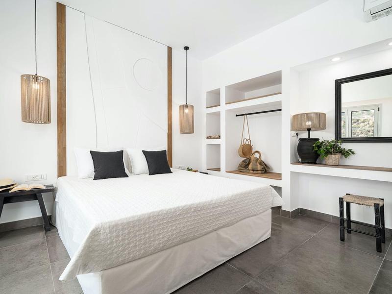 Moderne hotelkamer met tweepersoonsbed, krukjes en open kledingkast.