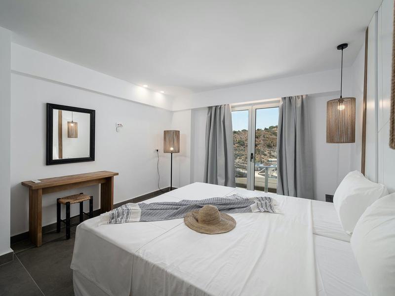 Lichte hotelkamer met tweepersoonsbed, twee lampen en raam met uitzicht op heuvels.