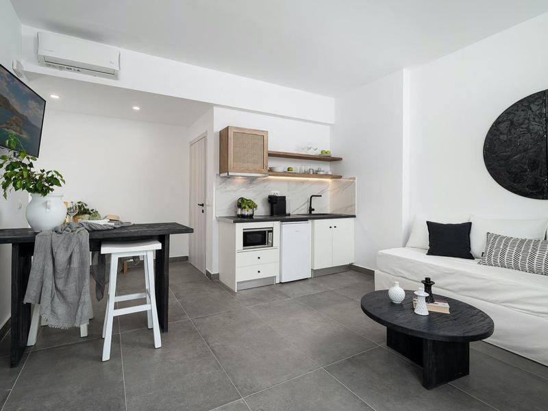 Moderne, lichte woonkamer met kitchenette, bank en tv in neutrale kleuren.