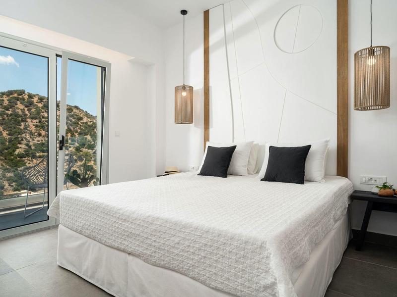 Modern ingerichte slaapkamer met tweepersoonsbed, witte muren en uitzicht op berglandschap.