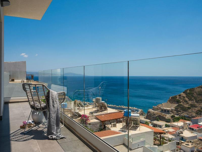 Balkon met stoelen en glazen balustrade met uitzicht op de zee en huizen op de heuvel.