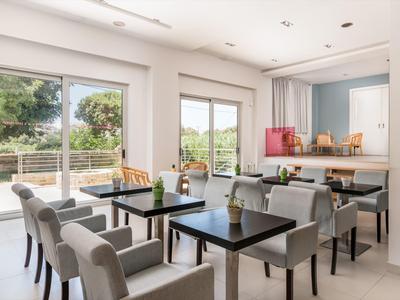 Heller Essbereich mit grauen Stühlen, schwarzen Tischen und großen Fenstern, die ins Grüne blicken.