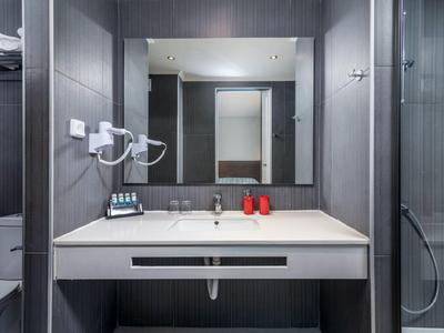 Moderner Badezimmerspiegel mit Waschbecken, Seifenspendern, Handtuchhaltern und dunklen Wandfliesen.