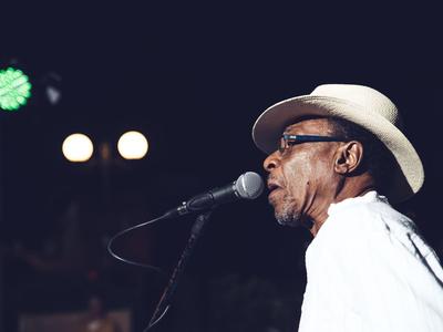 Un hombre con sombrero canta al micrófono en un escenario por la noche.