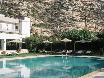 Piscina moderna con tumbonas y sombrillas junto a un edificio blanco frente a una colina rocosa.