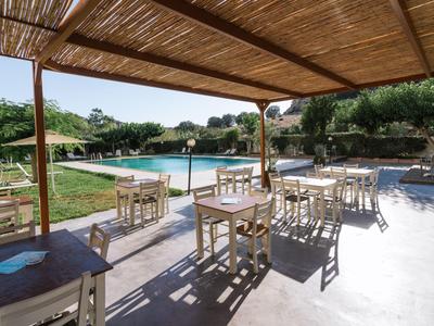 Zona de comedor cubierta con mesas y sillas junto a una piscina en un entorno verde.