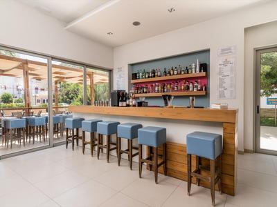 Moderner Hotelbarbereich mit blauen Hockern und Holzbar mit Regalen voller Getränke.