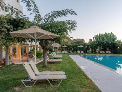 Pool mit Liegestühlen und Sonnenschirmen neben einem Hotelgebäude bei Sonnenuntergang.