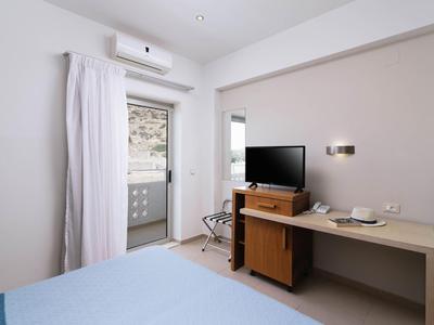 Ein helles Hotelzimmer mit Klimaanlage, Fernseher, Kühlschrank und Balkon.