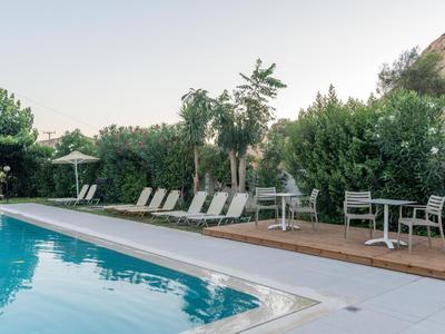 Hotelpool mit weißen Liegestühlen, Tischen und grüner Vegetation bei ruhiger Atmosphäre.